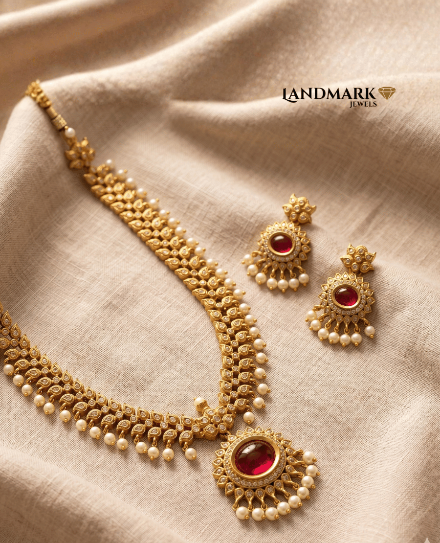 landmark-jewels-antique-gold-plated-necklace-and-earring-set-featuring-deep-red-ruby-stones-intricate-leaf-patterns-and-white-pearl-droplet-accents-resting-on-a-beige-linen-fabric