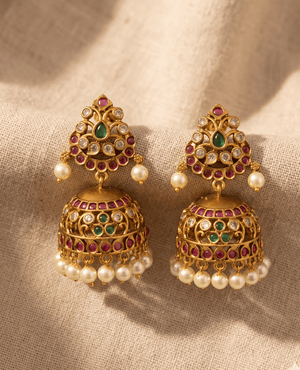 Traditional matte gold-plated Kundan jhumka earrings by Landmark Jewels, featuring intricate stone floral work, ruby and emerald centers, and a fringe of white faux pearls.