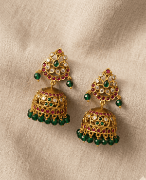 Antique matte gold temple-style jhumka earrings adorned with small ruby red and emerald green stones and hanging green beads.