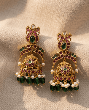 Ornate matte gold traditional jhumka earrings adorned with red and green stones and hanging green glass beads from Landmark Jewels.