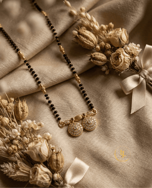 Landmark Jewels traditional gold-plated mangalsutra with black beads and dual diamond-studded circular pendant on a beige floral background.