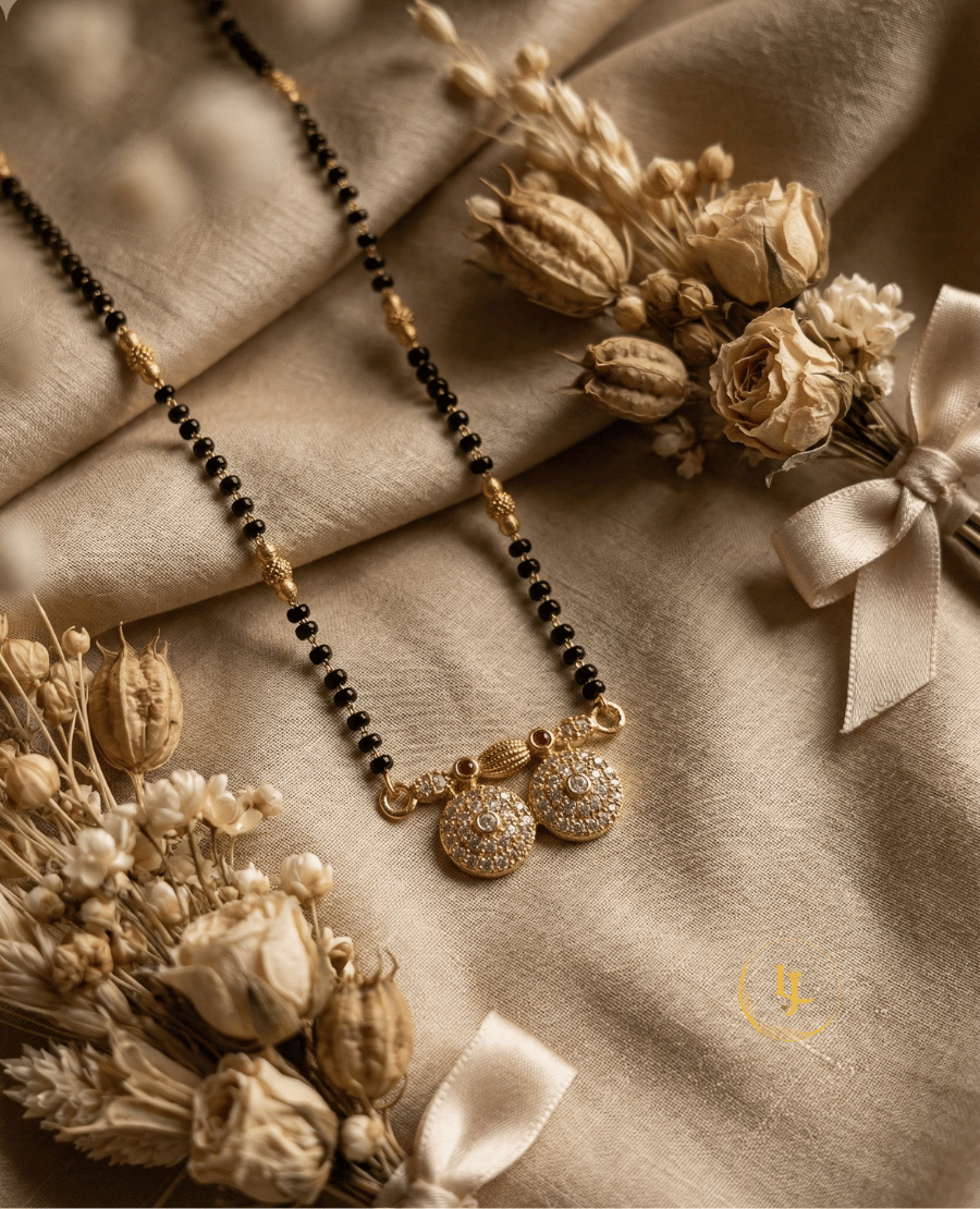landmark-jewels-traditional-gold-plated-mangalsutra-with-black-beads-and-dual-diamond-studded-circular-pendant-on-a-beige-floral-background