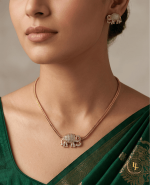Close-up of a model wearing a Landmark Jewels gold-toned elephant pendant necklace and matching stud earrings paired with a green silk saree.