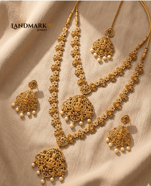 Landmark Jewels antique gold-plated temple jewelry set featuring Goddess Lakshmi pendants, red and green stones, and pearl hangings on a beige fabric background.