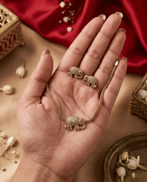 A hand holding a premium Landmark Jewels elephant necklace and earring set showing the delicate scale and sparkling white stone craftsmanship.