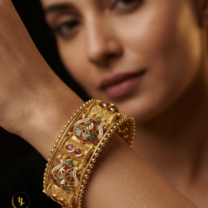 Pair of antique gold-plated Meenakari Kada bangles with green and red enamel work and ruby stone accents on a beige silk background.