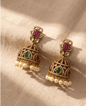 Pair of traditional antique gold-plated jhumka earrings featuring ruby, emerald stones, and hanging pearls by Landmark Jewels.