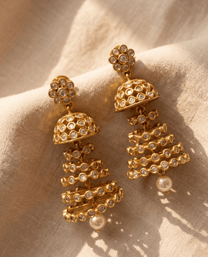Bold tiered chandelier style gold-plated jhumka earrings covered in clear cubic zirconia crystals with a hanging pearl.