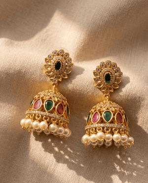 Traditional heavy gold bell-shaped Jhumka earrings by Landmark Jewels with alternating green and red teardrop stones and a thick cluster of hanging pearls.