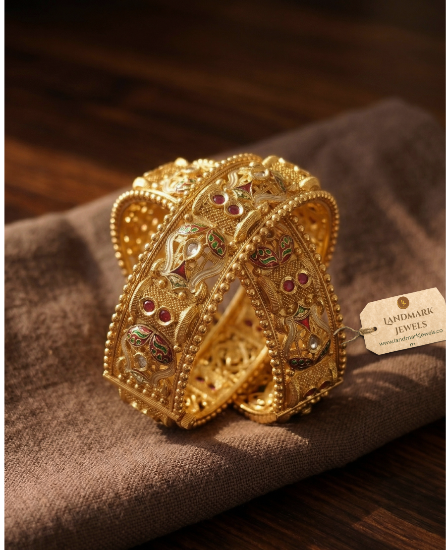 pair-of-antique-gold-plated-meenakari-kada-bangles-with-green-and-red-enamel-work-and-ruby-stone-accents-on-a-beige-silk-background