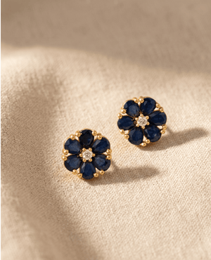 A pair of delicate gold-plated flower stud earrings featuring six pear-shaped dark blue sapphire stones surrounding a central bright white crystal.