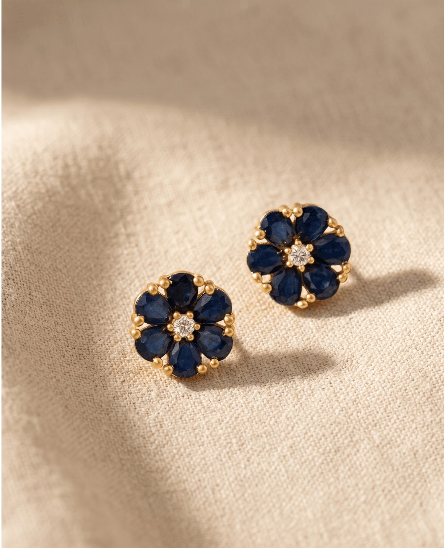 a-pair-of-delicate-gold-plated-flower-stud-earrings-featuring-six-pear-shaped-dark-blue-sapphire-stones-surrounding-a-central-bright-white-crystal