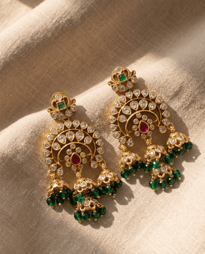 Elaborate gold Kundan chandbali earrings featuring three dangling jhumkas and emerald green glass beads.