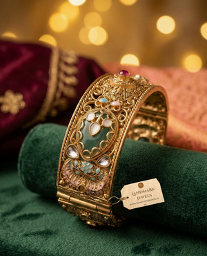 Pair of broad antique gold-plated Kada bangles with green Meenakari enamel work, Kundan stones, and floral details on a velvet display.