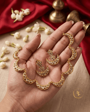 A hand holding a celestial-inspired gold necklace with white Kundan stone moon charms and matching earrings.