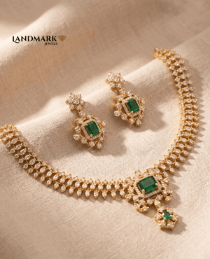 Landmark Jewels imitation jewelry set featuring a gold-toned necklace with emerald-cut green stones and leaf-shaped diamond accents, accompanied by matching floral halo earrings on a neutral fabric background.