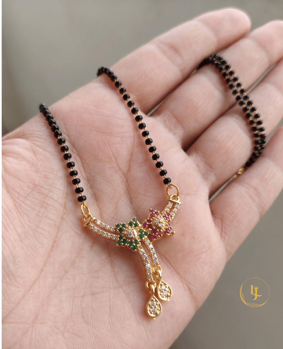 landmark-jewels-gold-plated-short-mangalsutra-with-floral-american-diamond-pendant-green-and-pink-stones-and-traditional-black-beads-on-a-beige-fabric-background