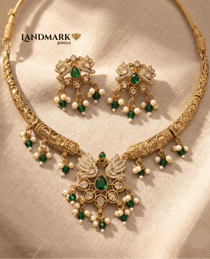 Landmark Jewels traditional gold-plated necklace and earring set featuring a peacock motif pendant with emerald green pear-shaped stones, white AD stone embellishments, and hanging pearl and green bead droplets on a neutral fabric background.