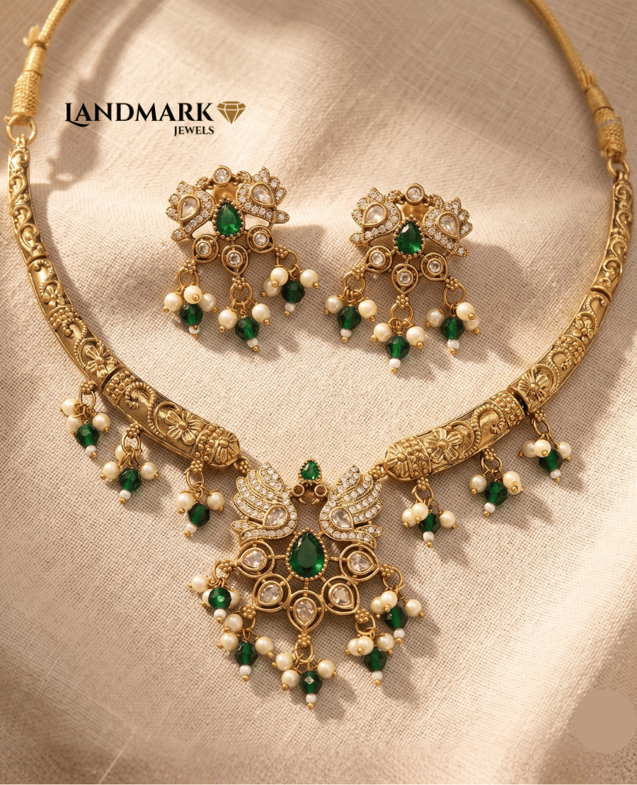 landmark-jewels-traditional-gold-plated-necklace-and-earring-set-featuring-a-peacock-motif-pendant-with-emerald-green-pear-shaped-stones-white-ad-stone-embellishments-and-hanging-pearl-and-green-bead-droplets-on-a-neutral-fabric-background