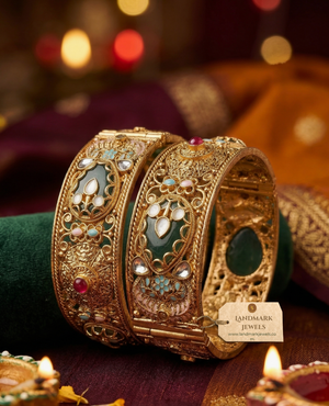 Pair of broad antique gold-plated Kada bangles with green Meenakari enamel work, Kundan stones, and floral details on a velvet display.