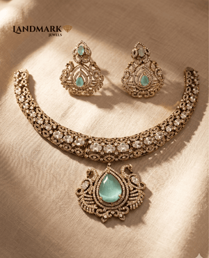 Landmark Jewels antique gold-finish necklace and earring set featuring mint green pear-shaped center stones and white polki-style accents on a textured beige background.