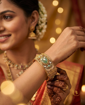 Pair of broad antique gold-plated Kada bangles with green Meenakari enamel work, Kundan stones, and floral details on a velvet display.