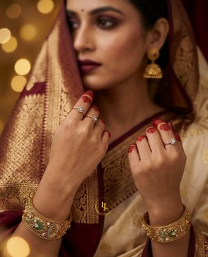 Pair of broad antique gold-plated Kada bangles with green Meenakari enamel work, Kundan stones, and floral details on a velvet display.