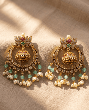 Ornate gold-toned crescent-style jhumka earrings by Landmark Jewels featuring a top lotus motif, a hanging inner jhumka bell, and a fringe of light green beads and white pearls.