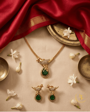 Top-down view of the Landmark Jewels emerald bird jewelry set arranged with jasmine flowers and red silk fabric.