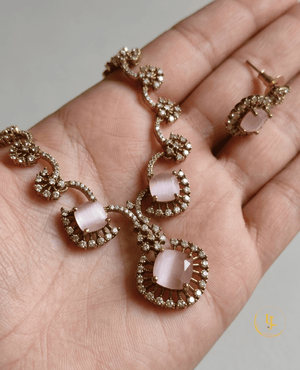 Handheld view of the pink cat's eye floral necklace by Landmark Jewels showing the intricate rose-gold craftsmanship.