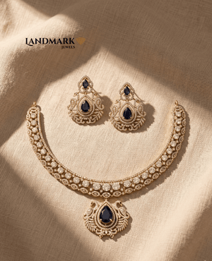 Landmark Jewels gold-plated necklace set featuring pear-cut blue sapphire stones and white CZ diamonds on a beige fabric background.
