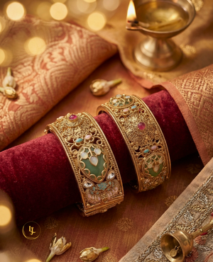 Pair of broad antique gold-plated Kada bangles with green Meenakari enamel work, Kundan stones, and floral details on a velvet display.