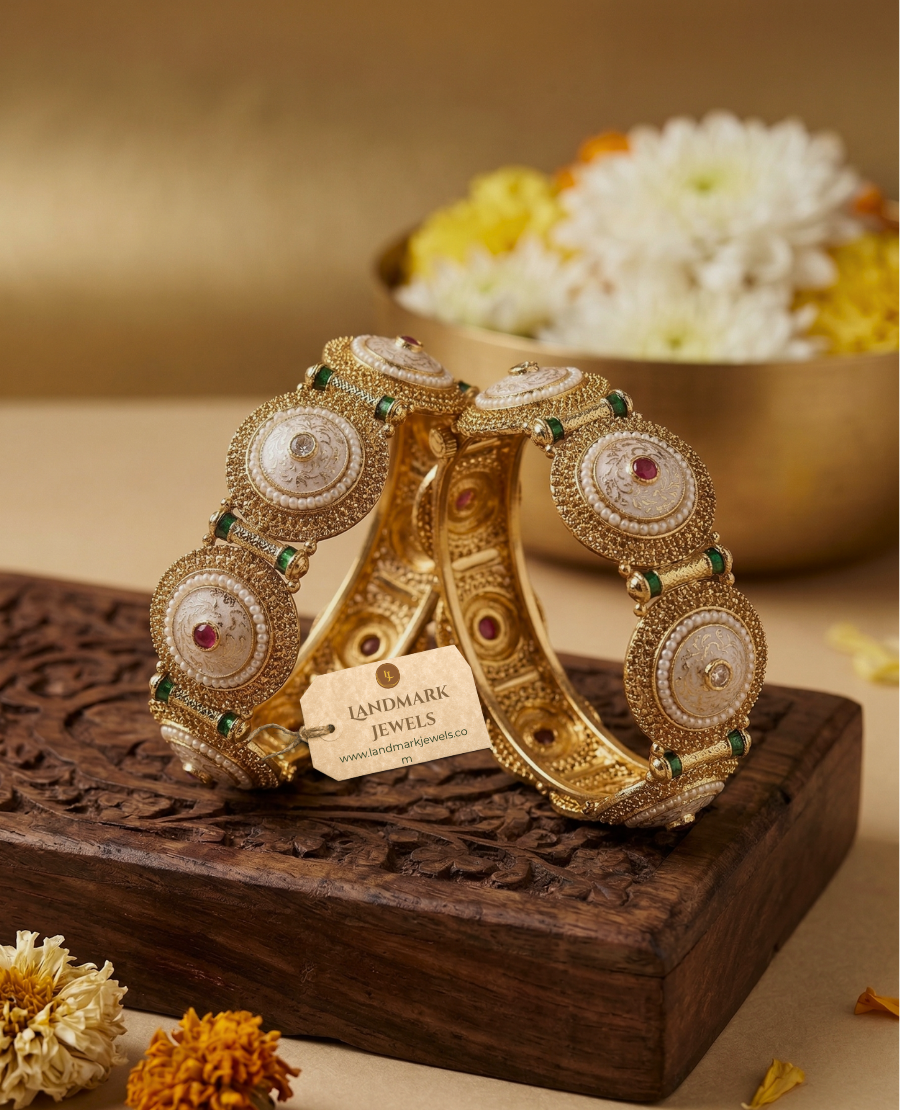 pair-of-antique-gold-plated-indian-kada-bangles-with-white-meenakari-enamel-work-pearls-and-red-stones-resting-on-a-carved-wooden-box-with-floral-background
