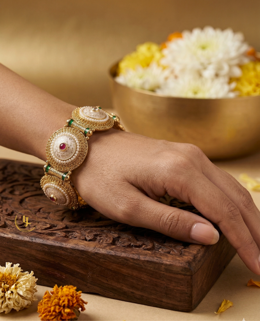 pair-of-antique-gold-plated-indian-kada-bangles-with-white-meenakari-enamel-work-pearls-and-red-stones-resting-on-a-carved-wooden-box-with-floral-background
