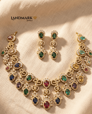 Landmark Jewels imitation jewelry set featuring a gold-toned choker necklace and drop earrings with multi-colored oval gemstones and white zirconia accents on a beige fabric background.