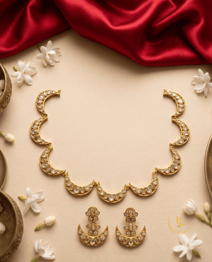 Flat lay of a crescent moon Kundan jewelry set on a beige background with red silk fabric and jasmine flowers.