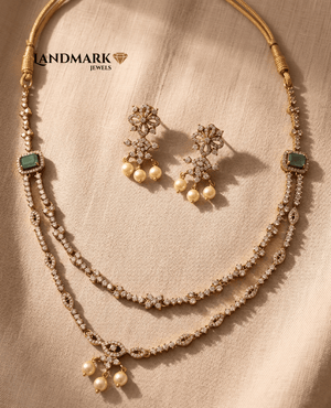  Landmark Jewels layered CZ necklace set with green emerald stones and pearl drops, including matching floral earrings, displayed on a textured beige fabric.