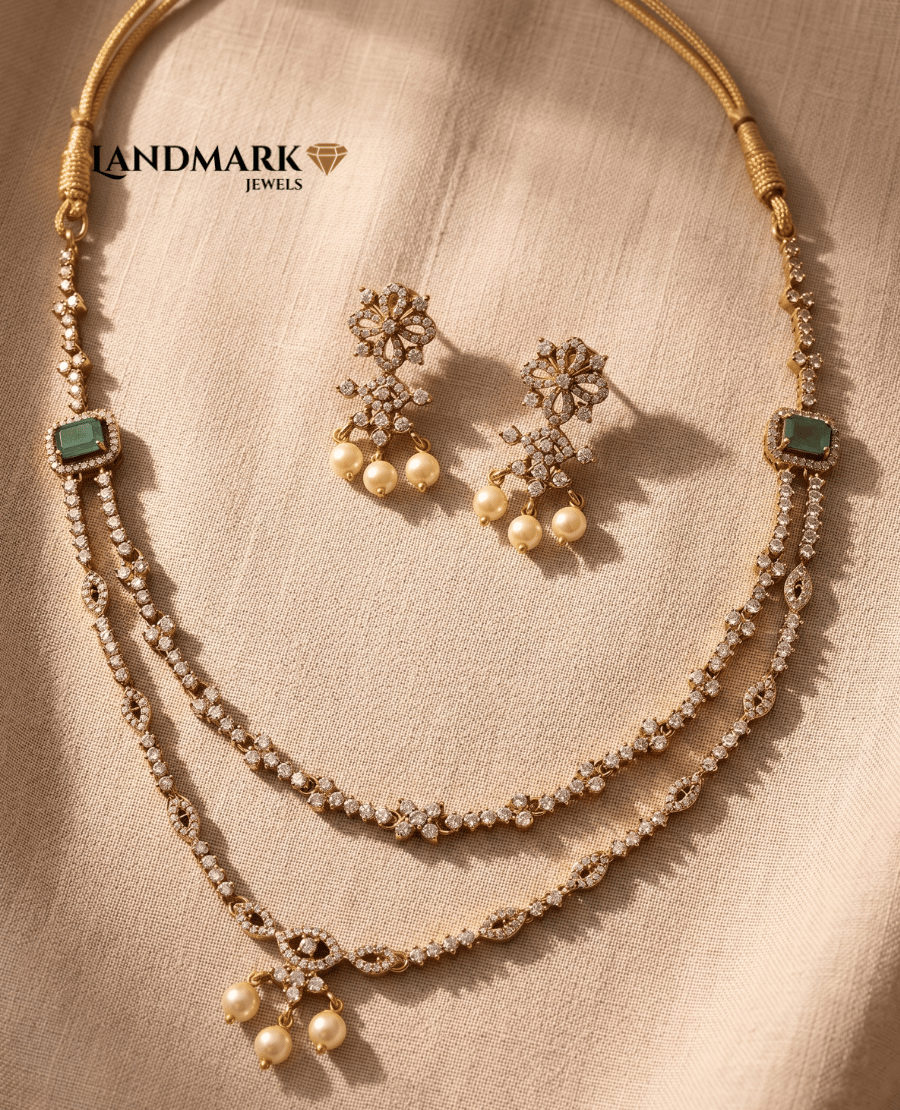 landmark-jewels-layered-cz-necklace-set-with-green-emerald-stones-and-pearl-drops-including-matching-floral-earrings-displayed-on-a-textured-beige-fabric