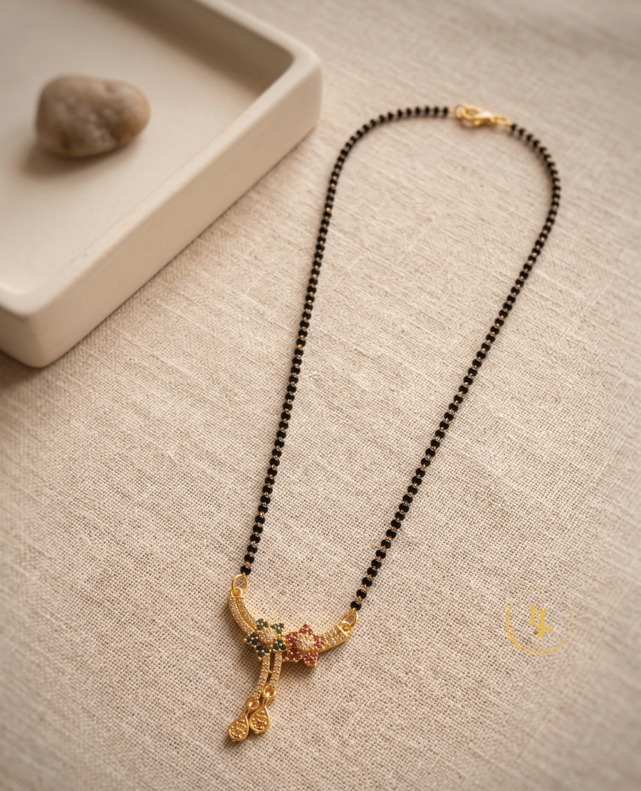 landmark-jewels-gold-plated-short-mangalsutra-with-floral-american-diamond-pendant-green-and-pink-stones-and-traditional-black-beads-on-a-beige-fabric-background