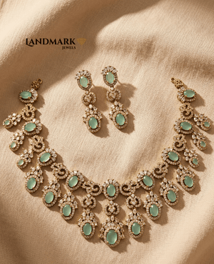 Landmark Jewels imitation jewelry set featuring a gold-toned necklace and earrings with oval mint green stones and white crystal embellishments on a beige fabric background.