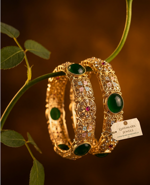 Antique gold-plated bangles with emerald green stones and floral Meenakari design on a traditional festive background.