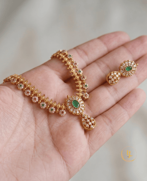 Close-up view of the intricate gold-plated floral detailing and emerald centerpiece of the Landmark Jewels necklace held in hand.
