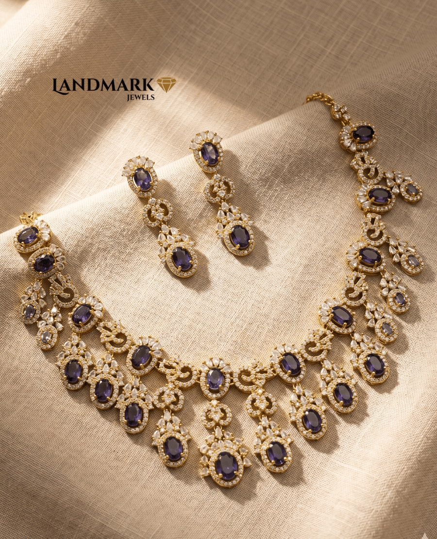 ornate-gold-plated-choker-necklace-and-drop-earrings-set-featuring-deep-purple-oval-gemstones-and-white-zircon-accents-by-landmark-jewels-displayed-on-a-textured-beige-fabric