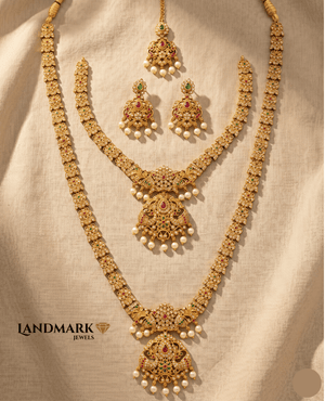 Landmark Jewels traditional antique gold-plated necklace set featuring a long haram, choker, jhumkas, and maang tikka with red and green stones and pearl drops.