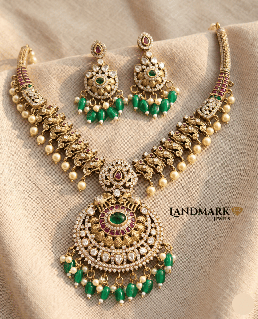 landmark-jewels-antique-gold-plated-necklace-and-earrings-set-featuring-emerald-green-stones-ruby-accents-and-pearl-droplets-on-a-beige-fabric-background