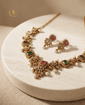 High-angle shot of a matte gold finish multicolor stone necklace and earring set displayed on a marble surface.