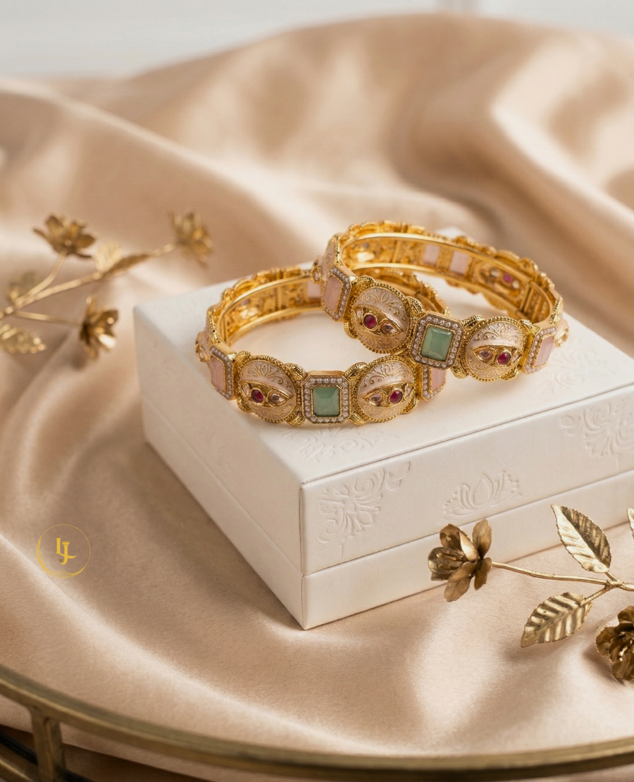 pair-of-gold-plated-indian-meenakari-bangles-with-ruby-and-emerald-stones-on-a-beige-fabric-background