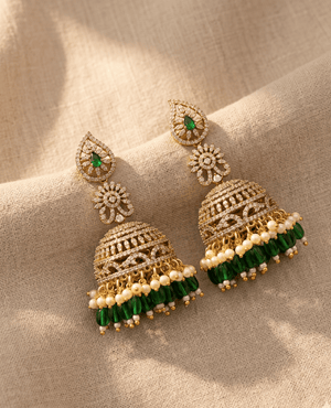 Pair of traditional, heavy gold-plated dome-shaped jhumka earrings by Landmark Jewels with a floral stud, brilliant crystal tiers, and a dense fringe of white pearls and green hanging beads.