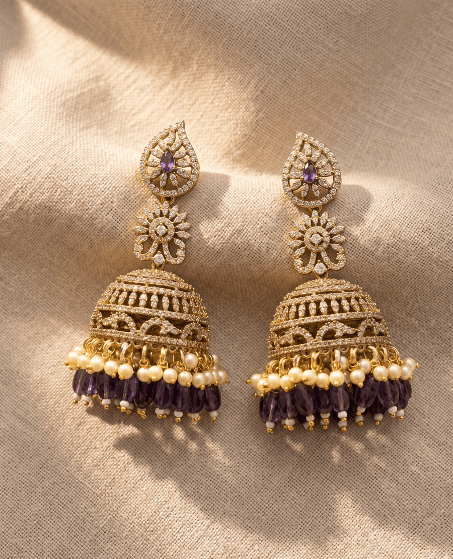 grand-tiered-gold-jhumka-earrings-featuring-a-paisley-top-with-a-purple-stone-an-intensely-detailed-crystal-dome-and-layered-fringes-of-white-pearls-and-purple-glass-beads
