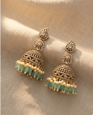 Heavy bridal-style gold-plated jhumka earrings featuring intricate cz filigree work and a dangling row of mint green oval beads and pearls.